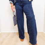 Person wearing blue jeans with decorative studs, a denim jacket, and brown shoes indoors.