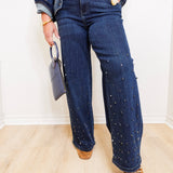 Person wearing blue jeans with decorative studs, a denim jacket, and brown shoes indoors.