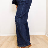 Person wearing dark blue jeans with decorative studs on a light wooden floor.