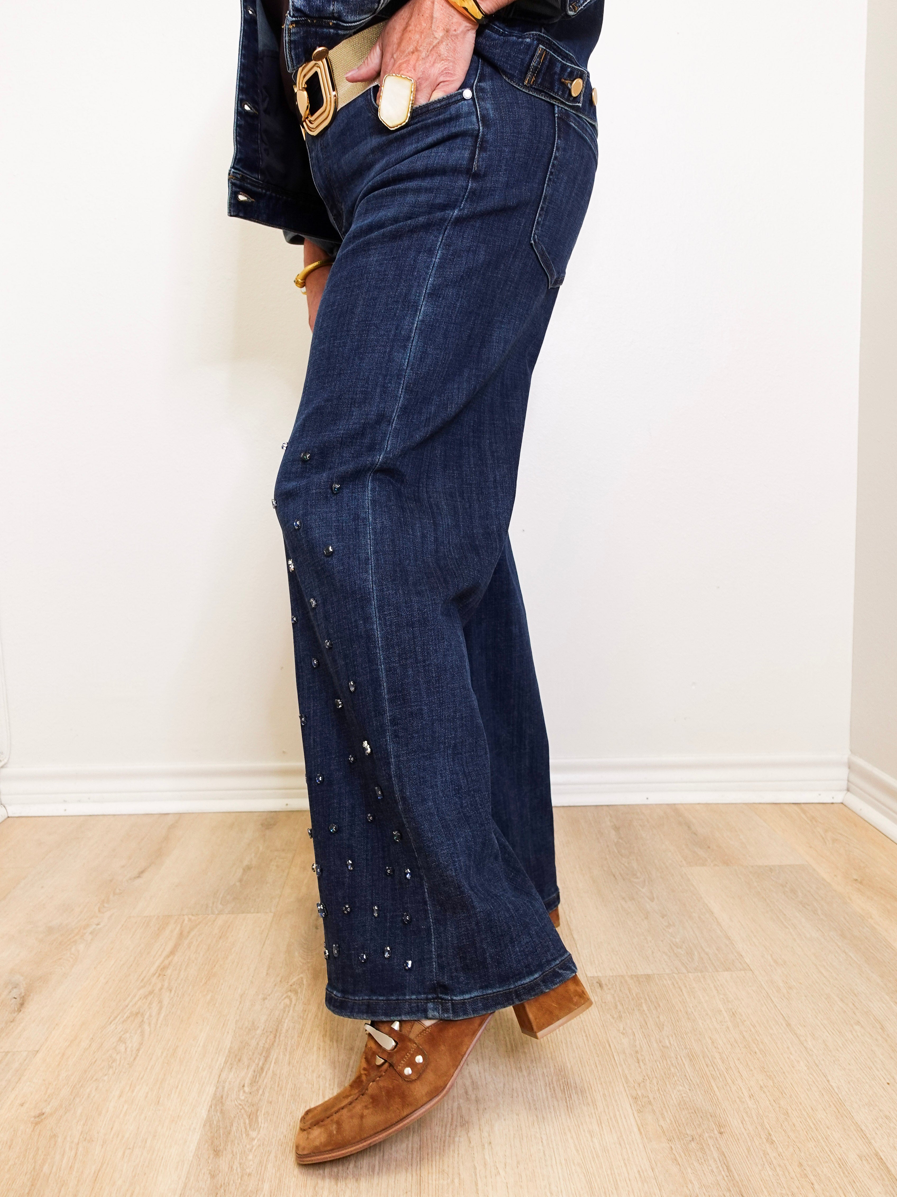 Person wearing dark blue jeans with decorative studs on a light wooden floor.