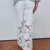 Person wearing a patterned sweater and white pants with lace details on a plain background