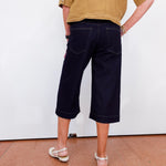 Person wearing navy capri pants and a mustard shirt against a white wall.