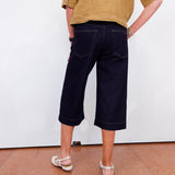 Person wearing navy capri pants and a mustard shirt against a white wall.