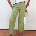 Person wearing green pants and a striped shirt, standing against a white wall.