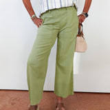 Person wearing green pants and a striped shirt, standing against a white wall.
