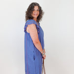 Woman wearing a blue dress with red stripes, standing against a white wall.