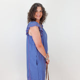 Woman wearing a blue dress with red stripes, standing against a white wall.