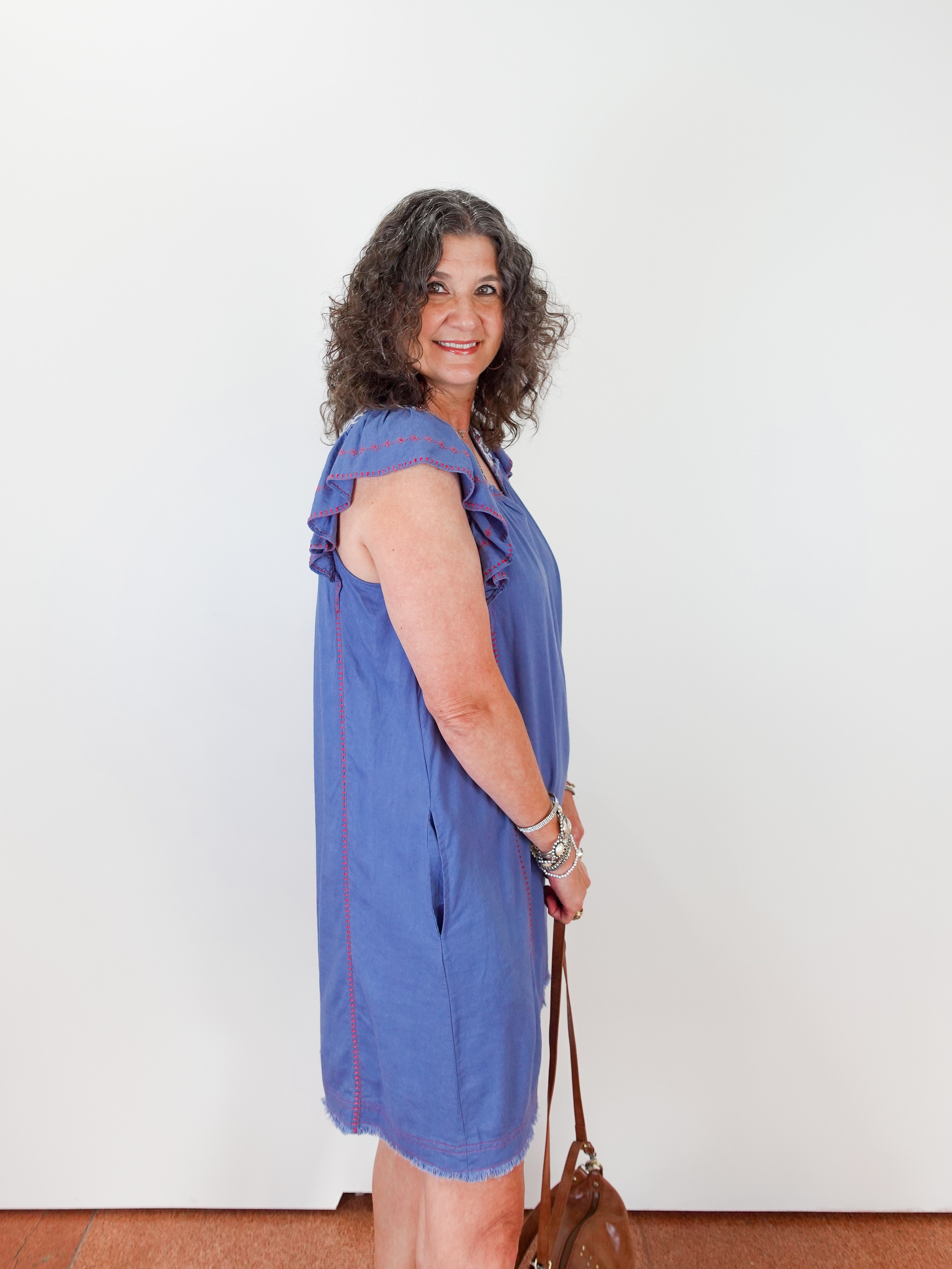 Woman wearing a blue dress with red stripes, standing against a white wall.