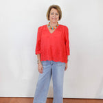 Woman wearing a red blouse and blue jeans against a white wall.