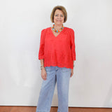 Woman wearing a red blouse and blue jeans against a white wall.