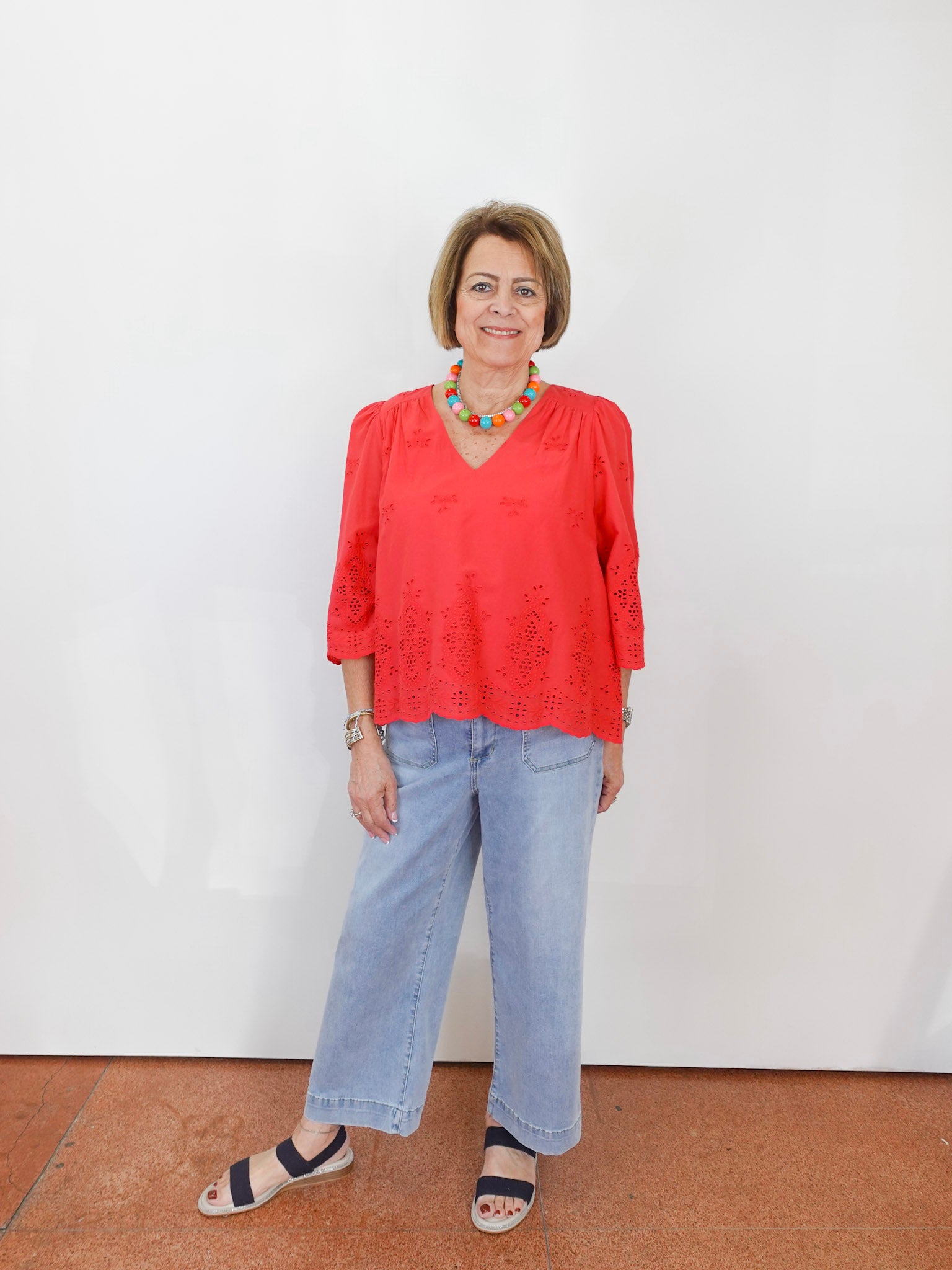 Woman wearing a red blouse and blue jeans against a white wall.