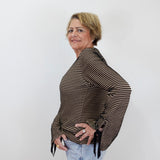 A woman with short blonde hair models a brown and black striped long-sleeve top with tie details at the cuffs, paired with light blue jeans, against a plain white background.