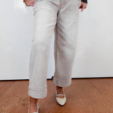 Person wearing light gray pants and white shoes on a brown floor with a white wall background