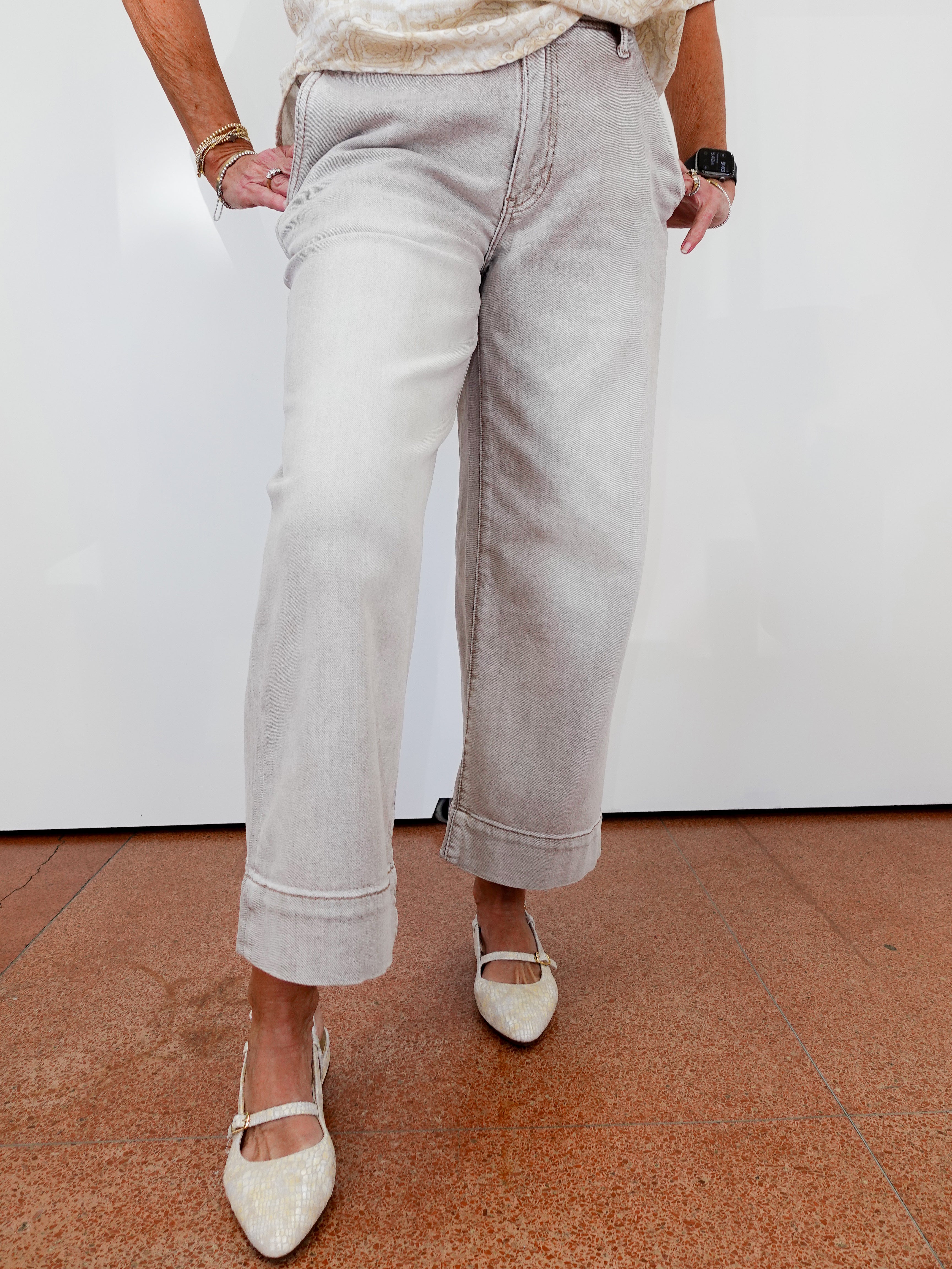 Person wearing light gray pants and white shoes on a brown floor with a white wall background