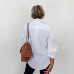 Person wearing a white shirt and black pants with a brown leather bag on a plain background