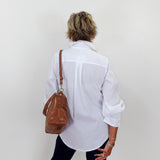 Person wearing a white shirt and black pants with a brown leather bag on a plain background