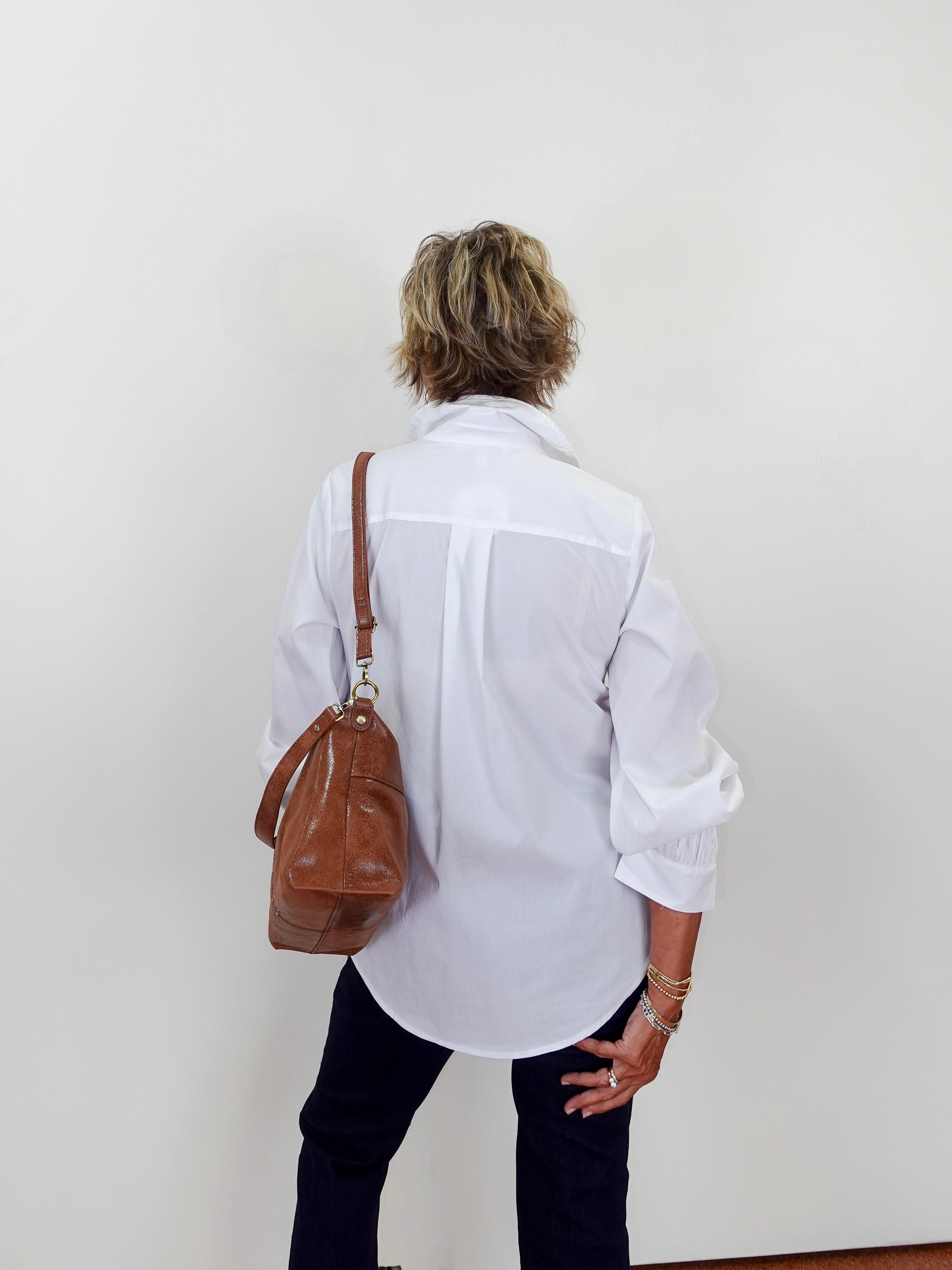Person wearing a white shirt and black pants with a brown leather bag on a plain background