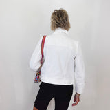 Person wearing a white jacket and black shorts with a colorful bag over one shoulder against a plain background