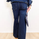 Person wearing a blue denim jacket and jeans holding a clutch against a white background