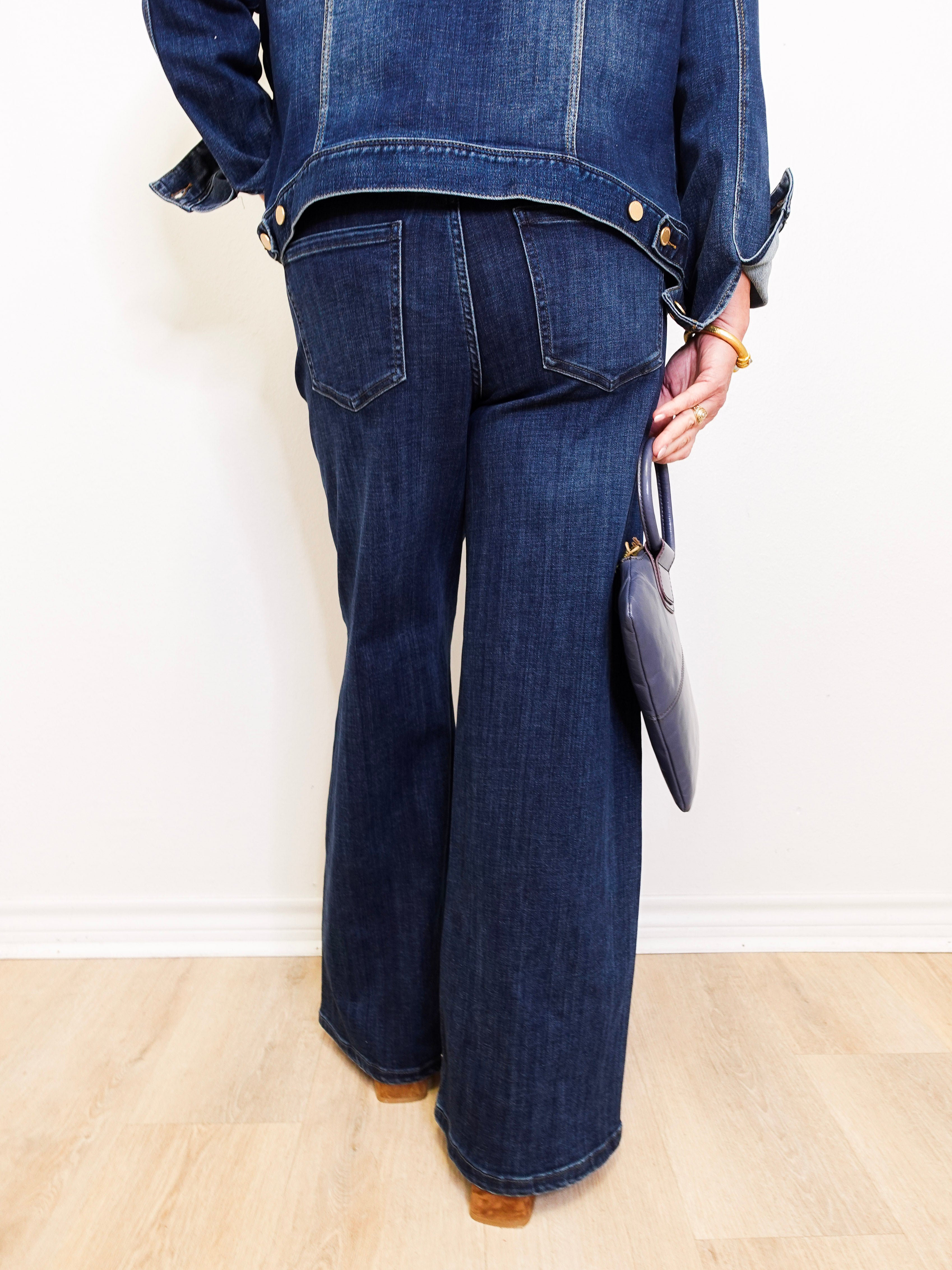 Person wearing a blue denim jacket and jeans holding a clutch against a white background