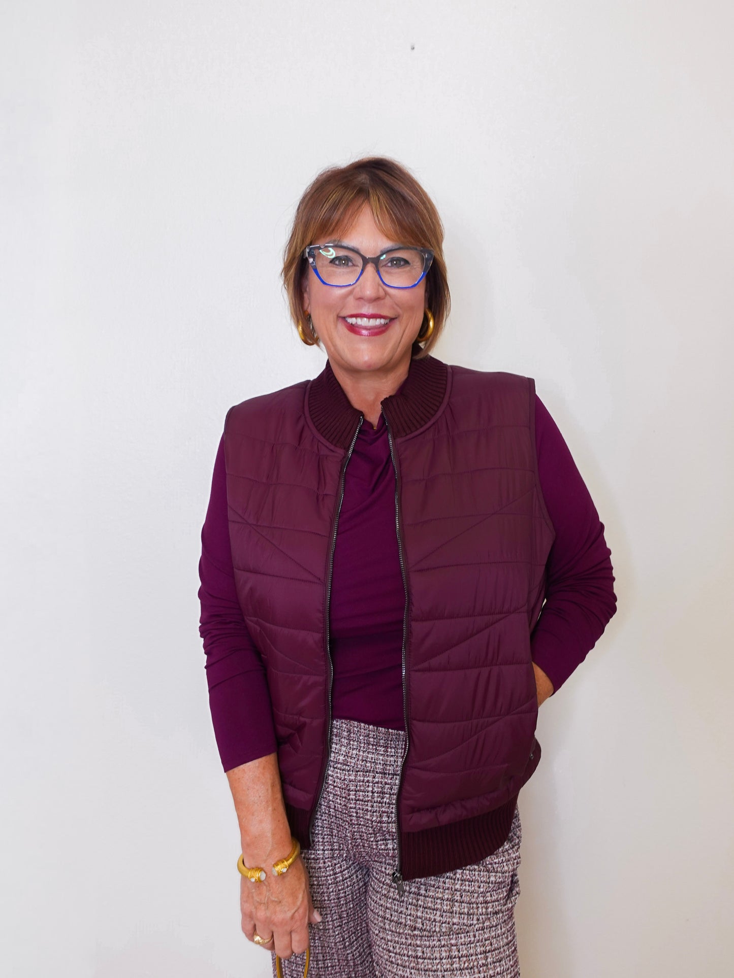 Woman wearing a purple vest over a purple shirt with a white background
