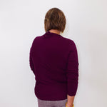 Person wearing a purple sweater and plaid pants against a white background