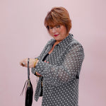 Woman wearing a patterned blazer holding a black handbag against a pink background