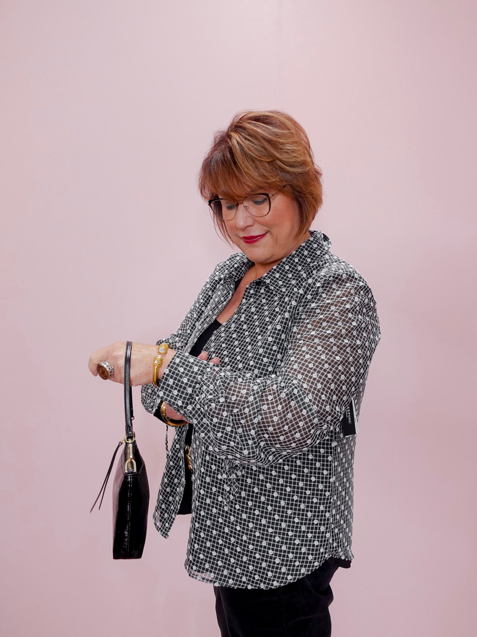 Woman wearing a patterned blazer holding a black handbag against a pink background