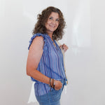 Woman wearing a blue striped shirt and jeans holding a white bag against a plain background