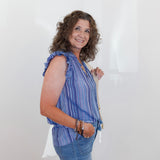 Woman wearing a blue striped shirt and jeans holding a white bag against a plain background