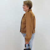 A woman in profile wearing a brown suede jacket with lace trim, light blue jeans, and holding a black handbag, standing against a plain white wall.