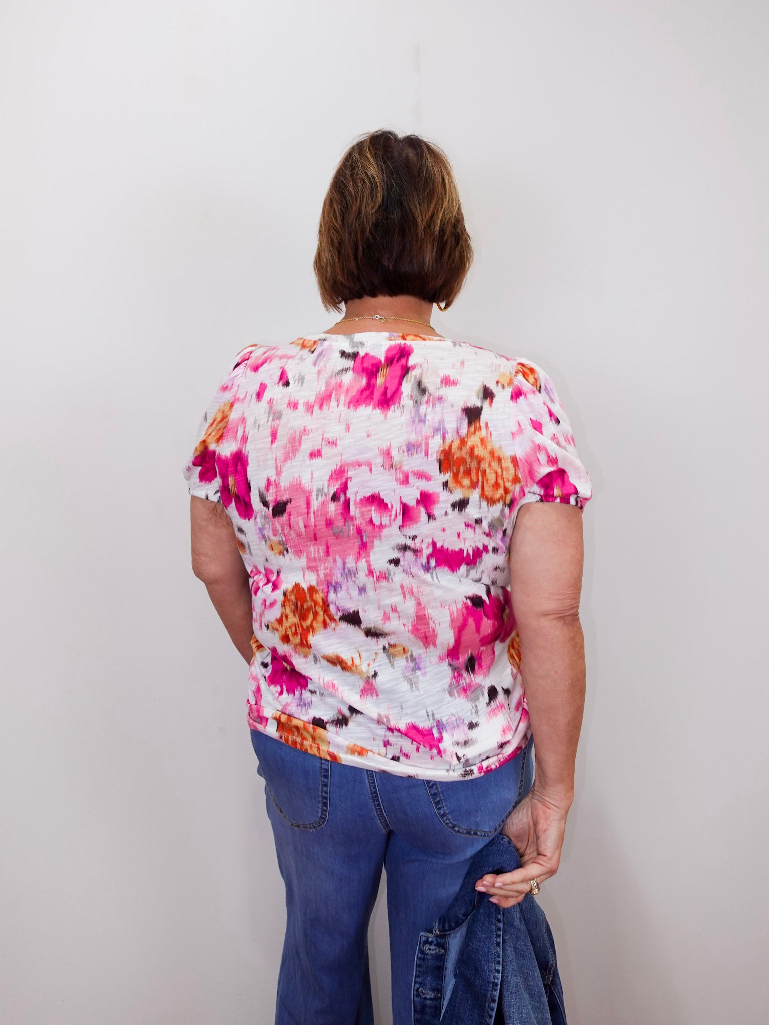 Person wearing a colorful floral shirt and blue jeans against a plain background