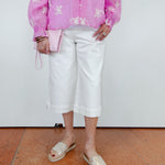 Person wearing a pink floral blouse, white pants, and beige sandals on a plain background