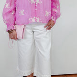 Person wearing a pink blouse with white floral patterns and white pants against a plain background