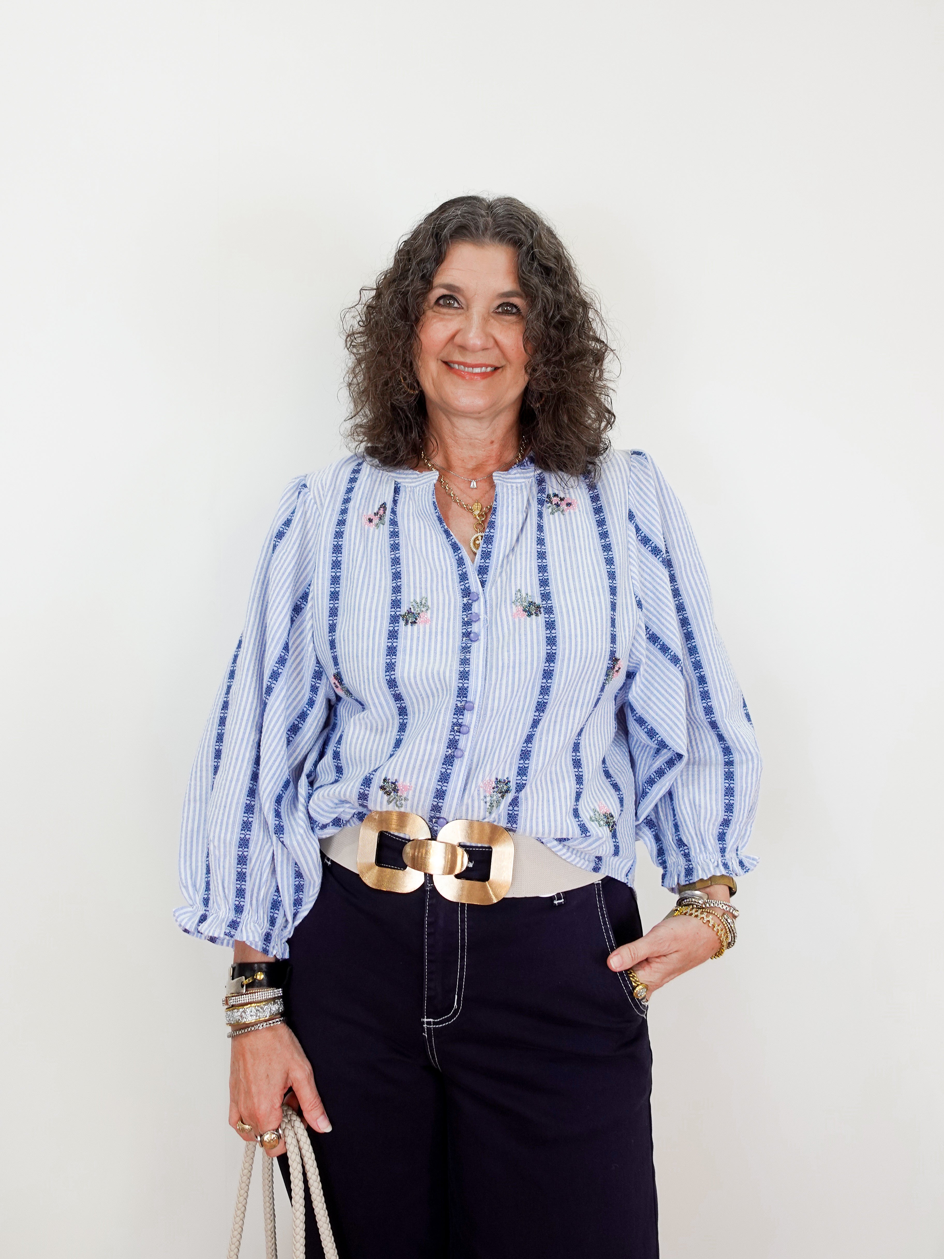 Woman wearing a blue and white striped shirt with a gold belt against a white background