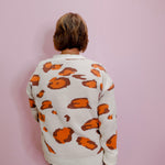 Person wearing a white sweater with orange patterns against a pink background