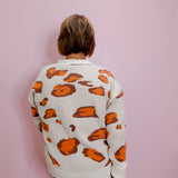 Person wearing a white sweater with orange patterns against a pink background