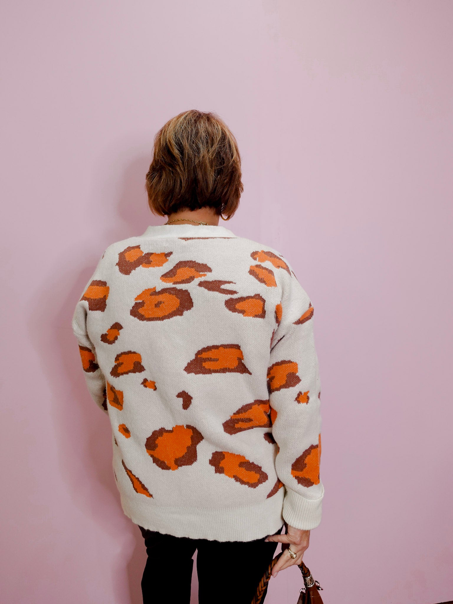 Person wearing a white sweater with orange patterns against a pink background