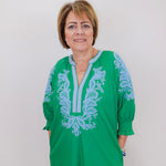 Woman wearing a green dress with blue embroidery against a white background