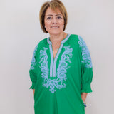 Woman wearing a green dress with blue embroidery against a white background