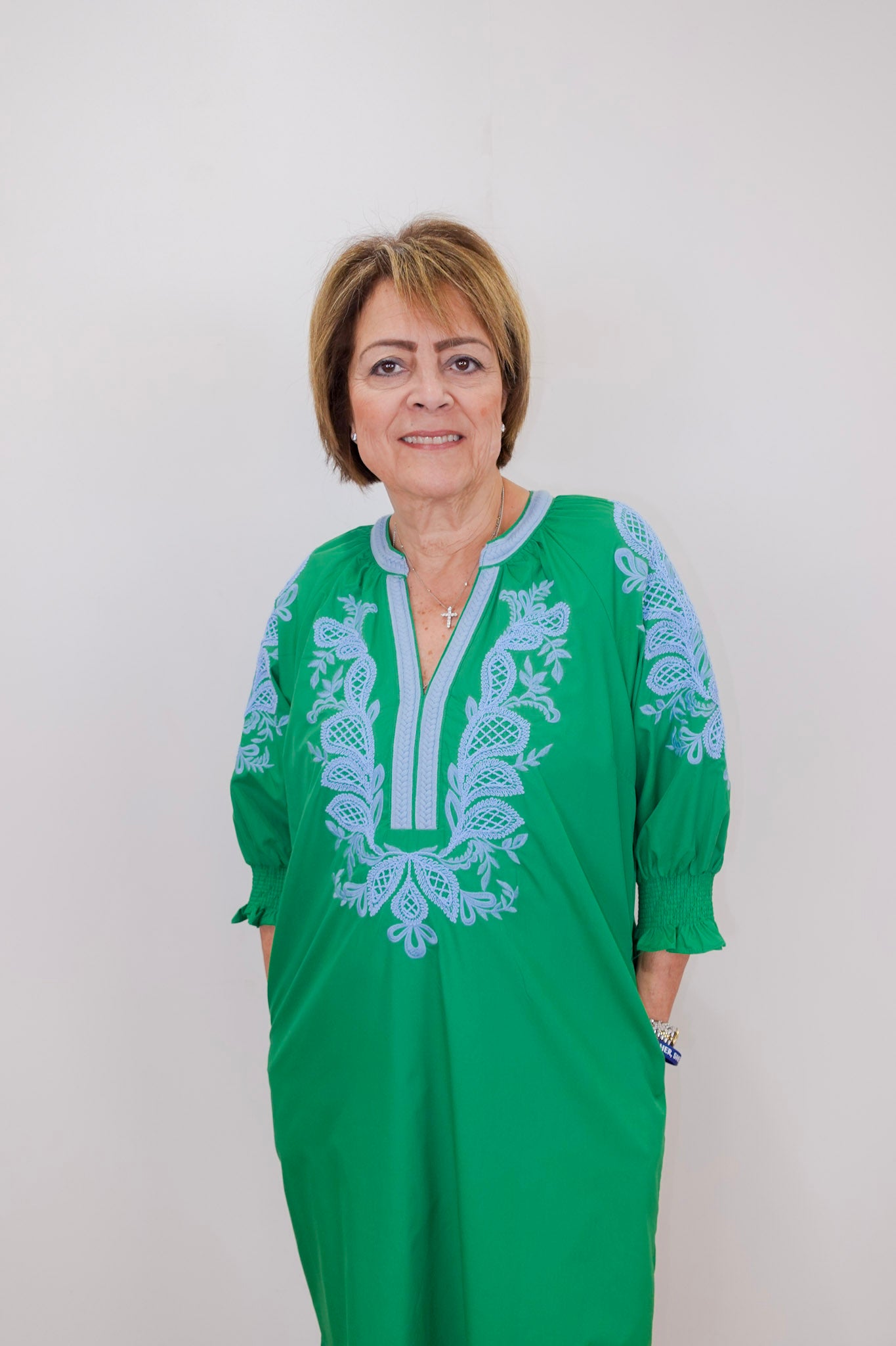Woman wearing a green dress with blue embroidery against a white background