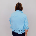 Woman wearing a light blue jacket with lace details on a plain background