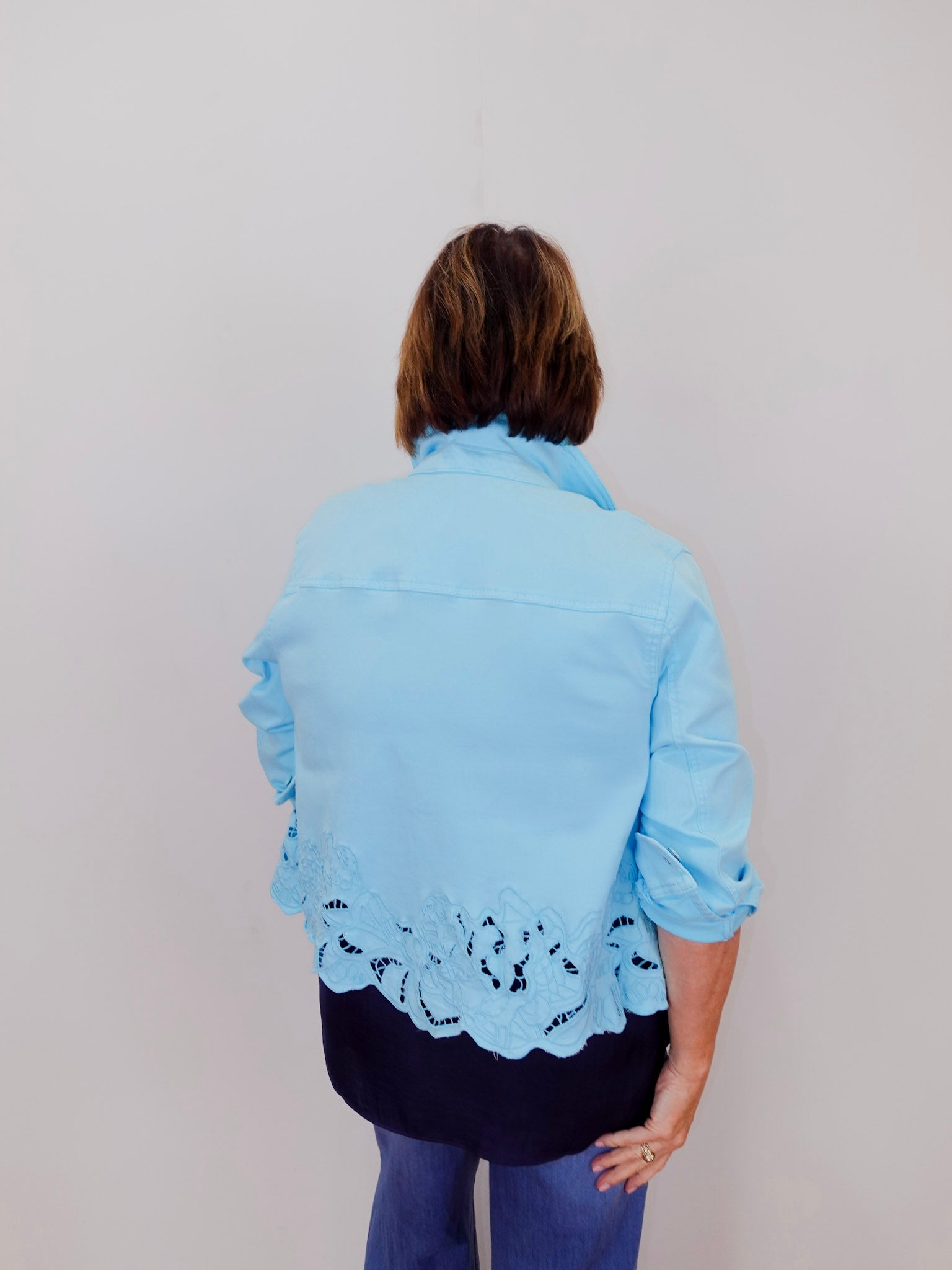 Woman wearing a light blue jacket with lace details on a plain background