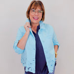 Woman wearing a light blue jacket with lace details on a plain background