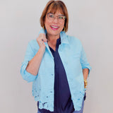 Woman wearing a light blue jacket with lace details on a plain background