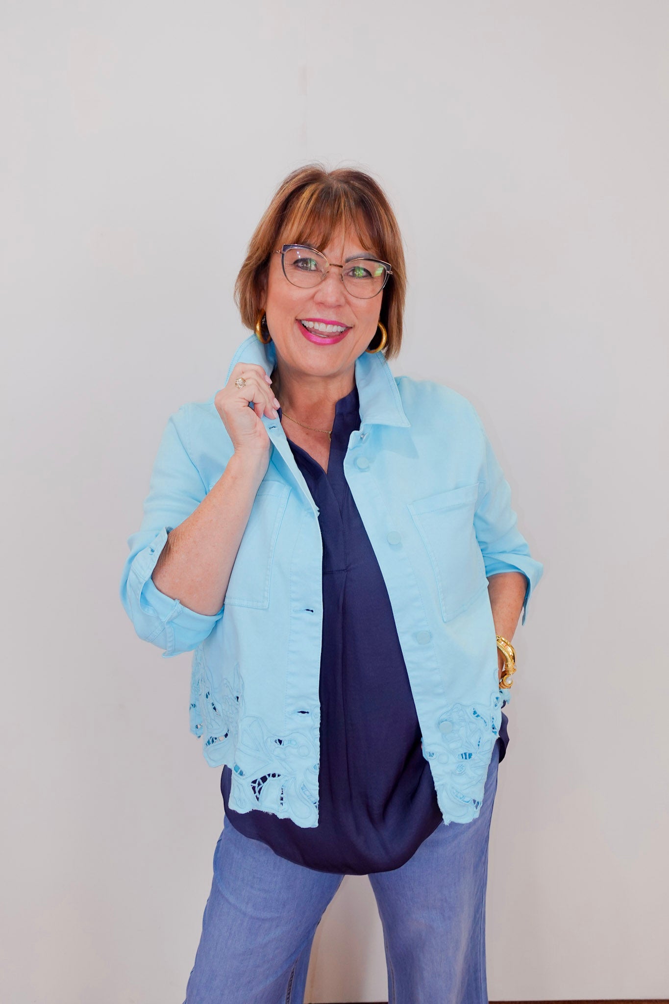 Woman wearing a light blue jacket with lace details on a plain background