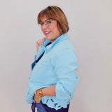Woman wearing a light blue jacket with lace details on a plain background
