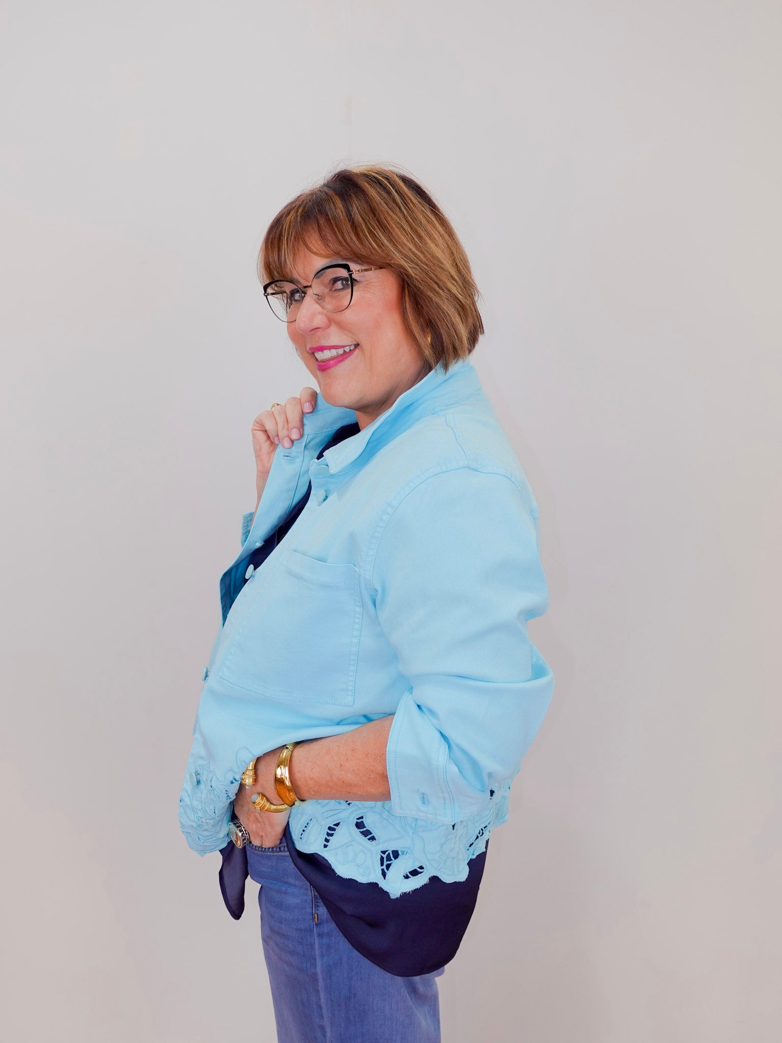 Woman wearing a light blue jacket with lace details on a plain background