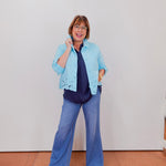 Woman wearing a light blue jacket with lace details on a plain background