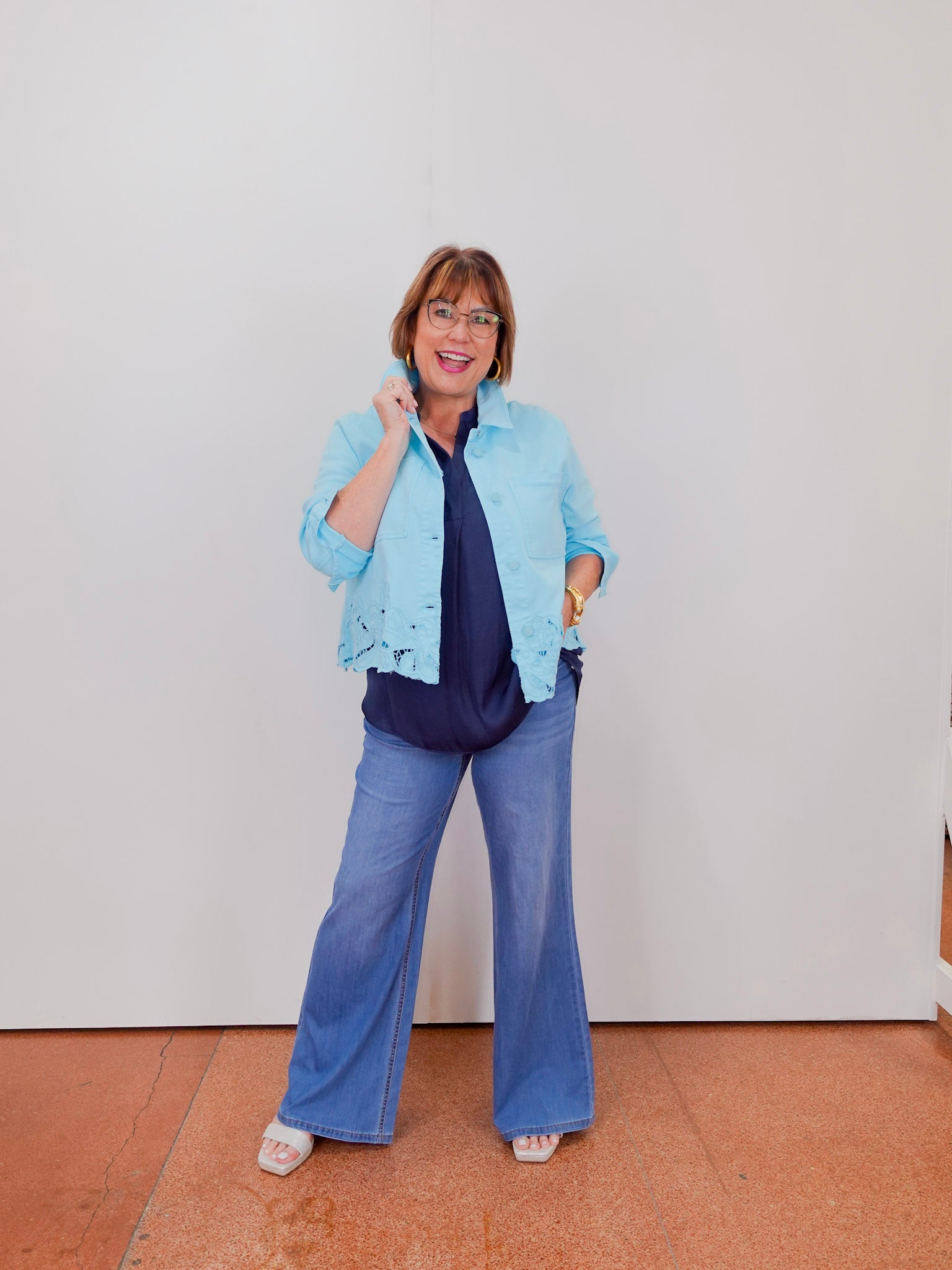 Woman wearing a light blue jacket with lace details on a plain background